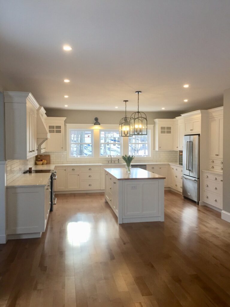 White kitchen with an island, lantern pendants and a wood floor