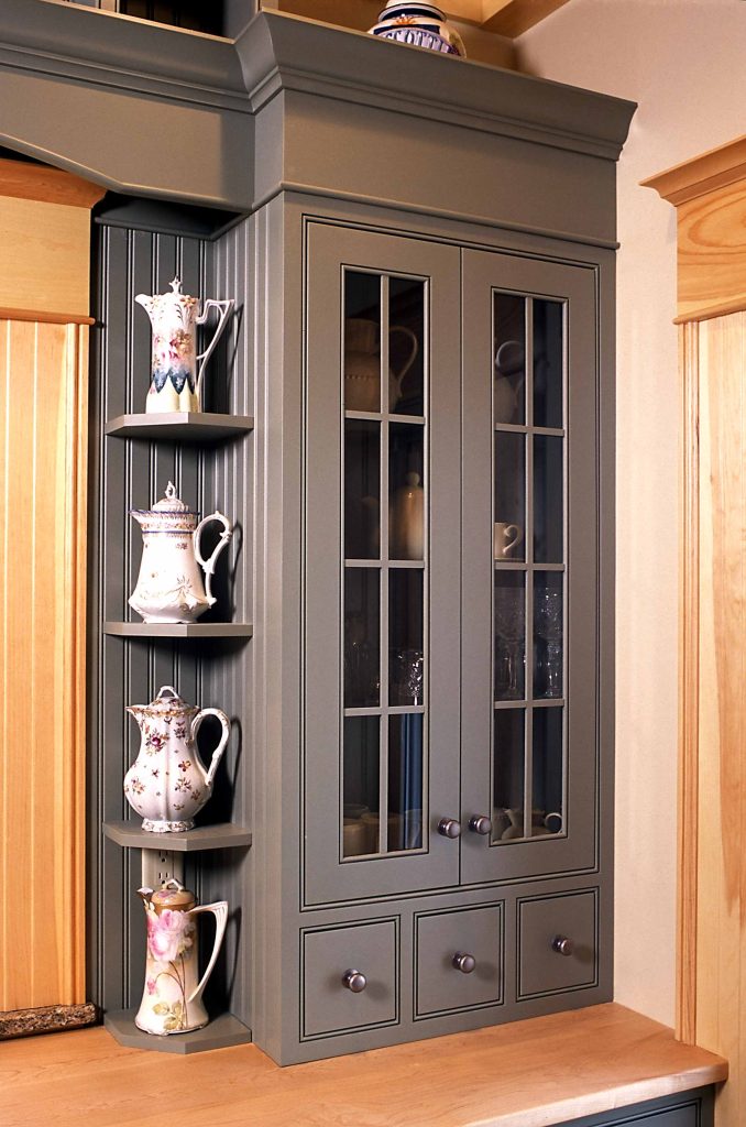 Blue-grey glass-front hutch with a curved open shelf holding teapots