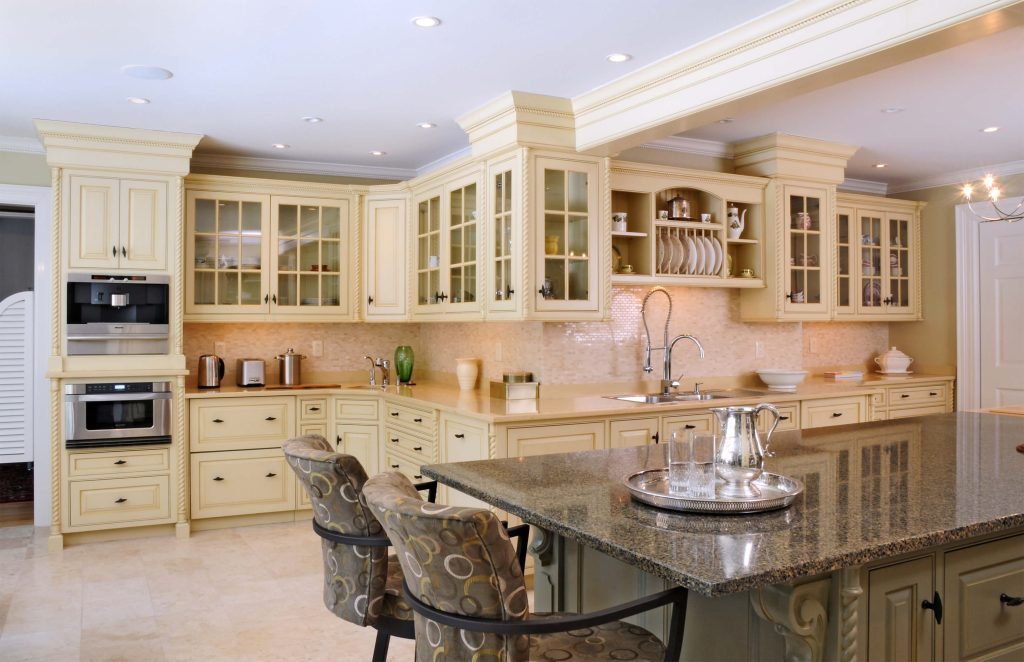 Cream painted kitchen with glass-front upper cabinets and a granite-topped sage island