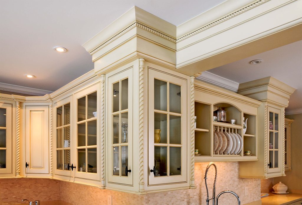 Cream upper cabinets with glass doors, crown moulding and a plate rack