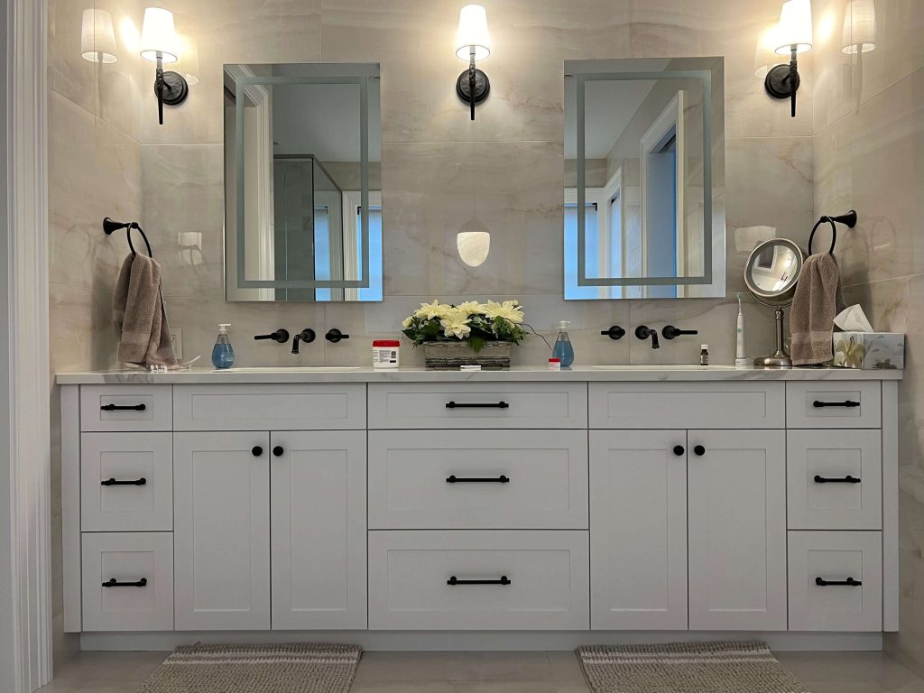 Ensuite with a grey double vanity, black faucets and wall sconces