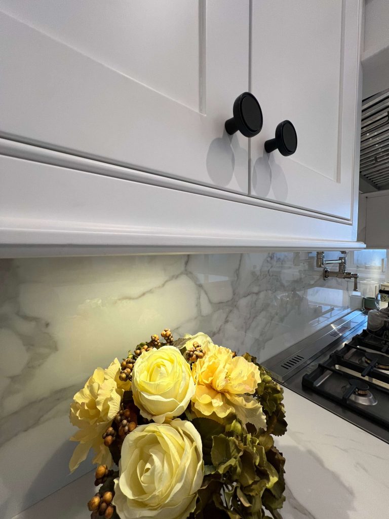 Black round knobs on white shaker cabinet doors above a marble backsplash