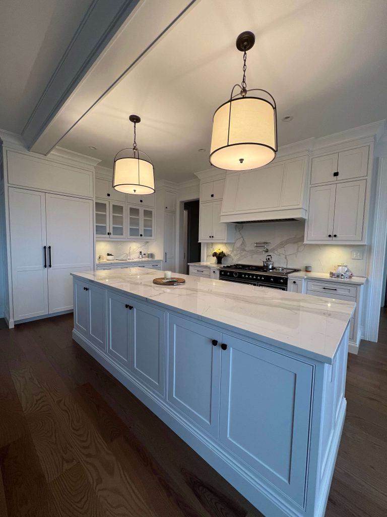 White kitchen with a long island, black hardware and a range wall with a white hood