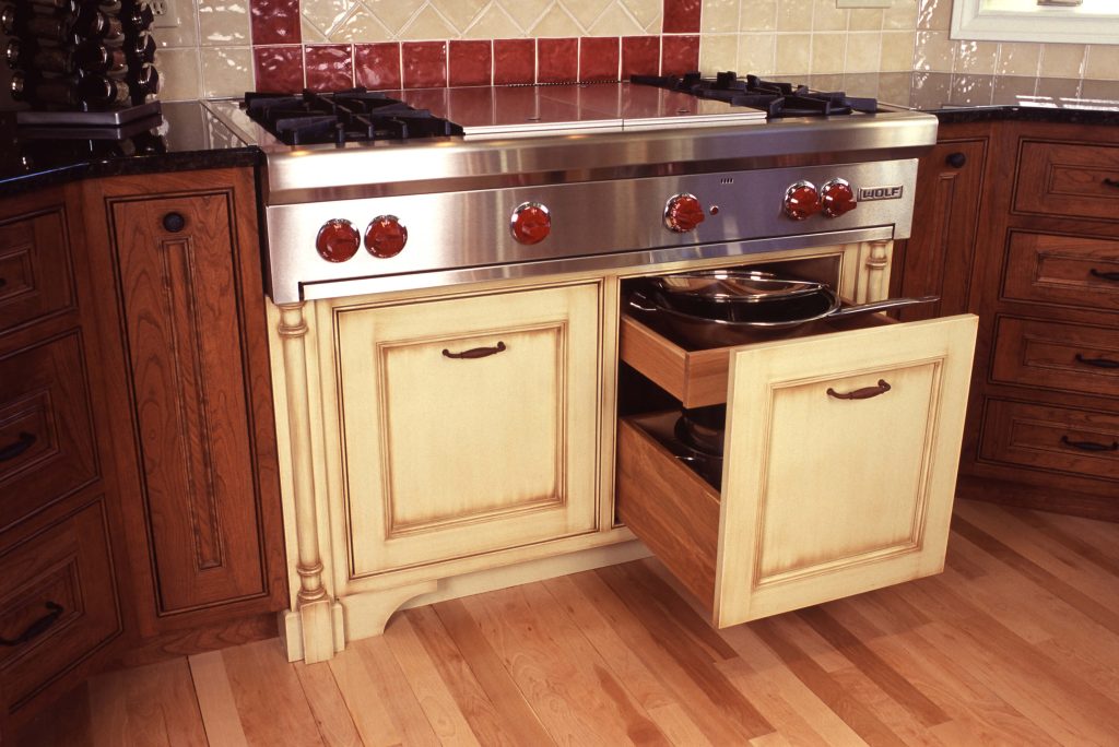 Cream cabinet with a pull-out drawer beneath a stainless range in a cherry kitchen