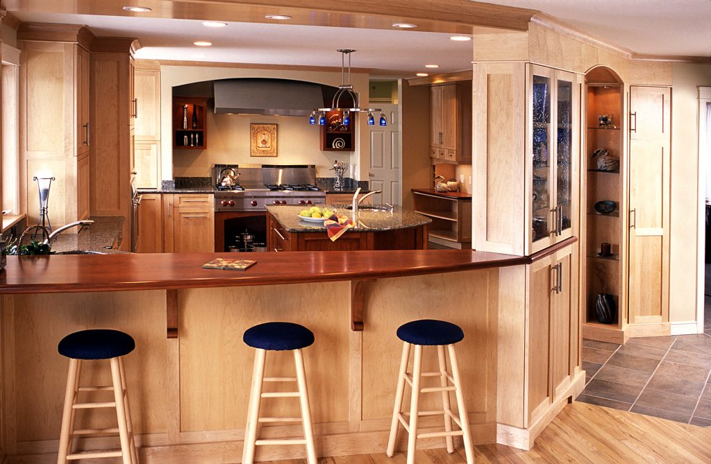 Maple kitchen seen across a cherry bar top with three stools