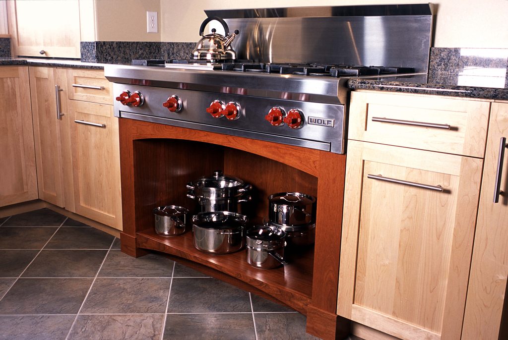 Professional rangetop above an arched cherry cabinet with open pot storage