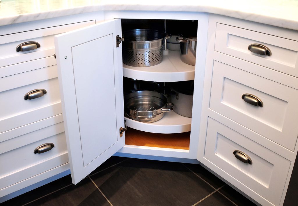 White corner cabinet with a lazy Susan holding pots