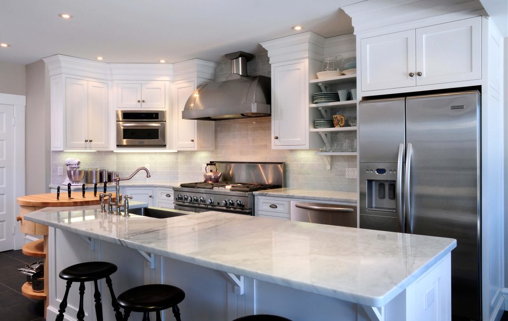 White kitchen with a marble island, stainless refrigerator and a butcher-block cart
