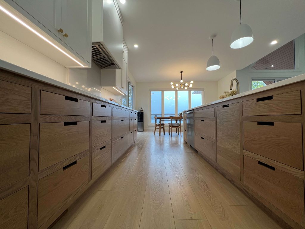 Oak drawer bank with black recessed pulls running the length of a kitchen