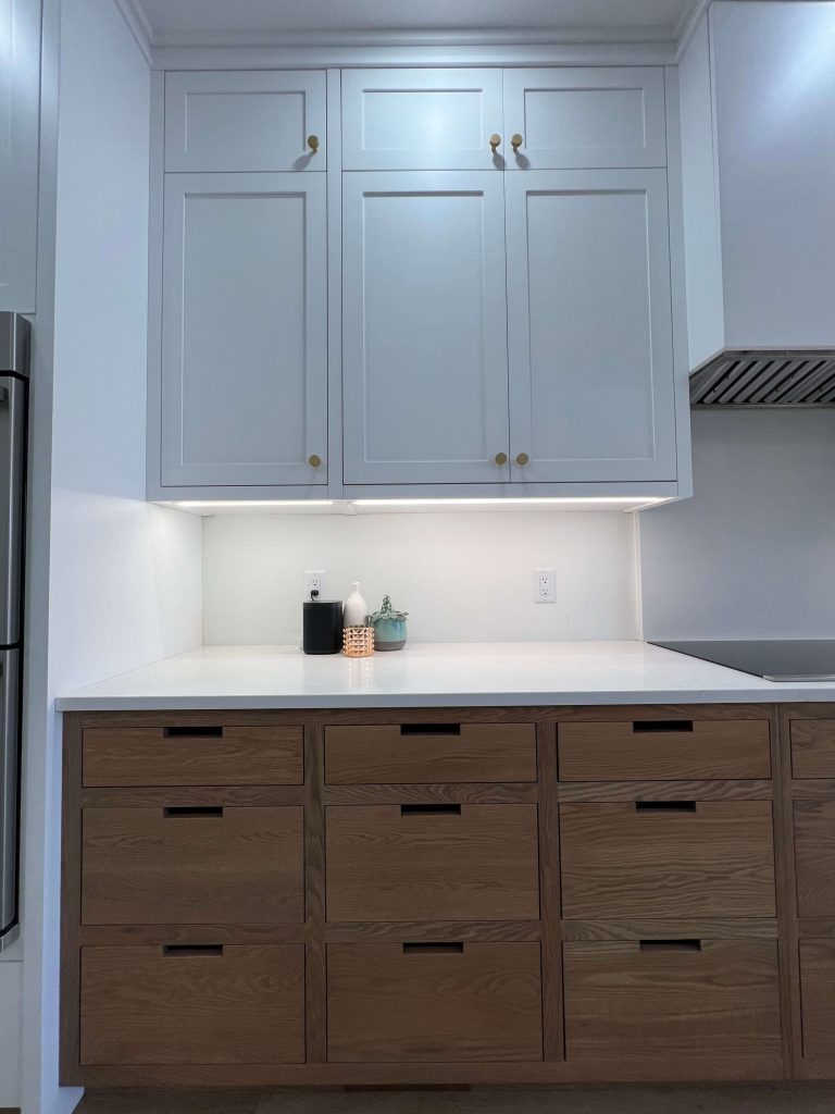 Oak drawers below white shaker upper cabinets with under-cabinet lighting