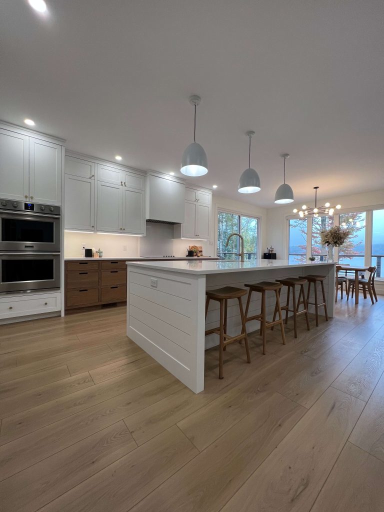Long kitchen with white upper cabinets, oak lower cabinets and a white island with seating