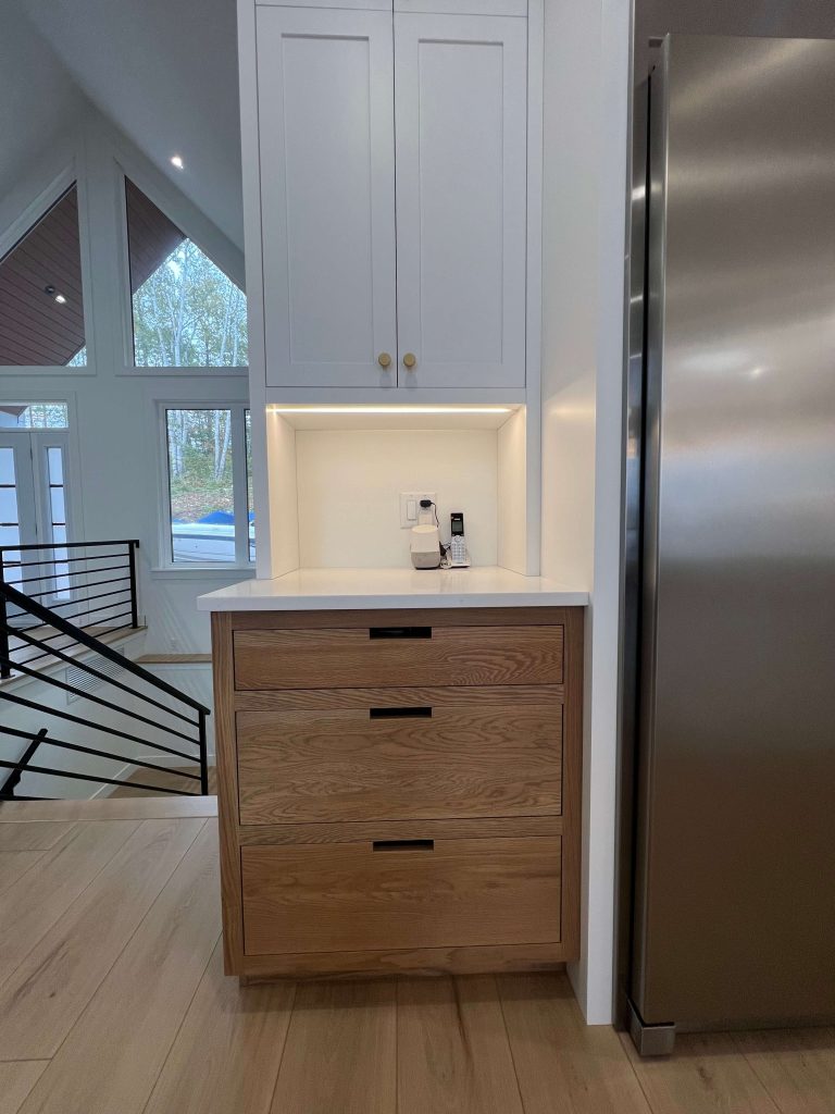 Coffee nook with oak drawers and a lit niche beside a stainless refrigerator