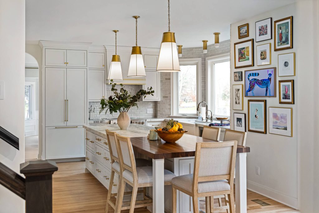 Bright white kitchen with brass pendant lights, a marble island and a walnut dining table