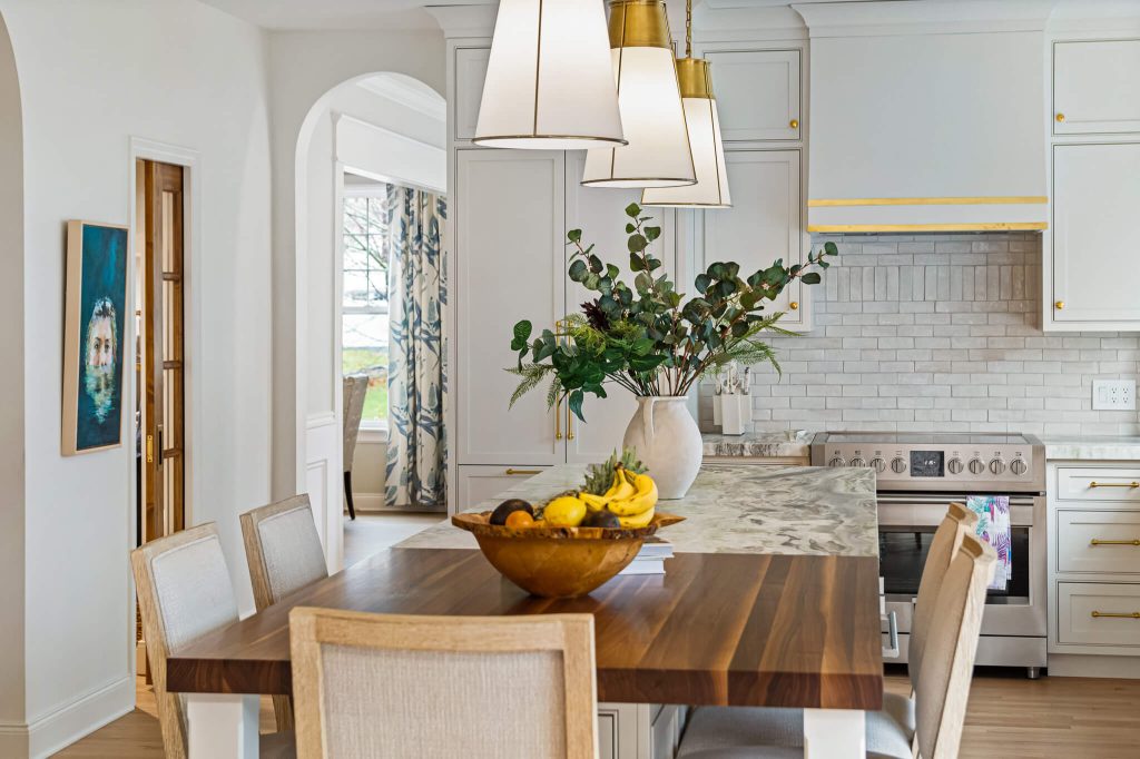 Walnut-topped table at the end of a white kitchen with a stainless range