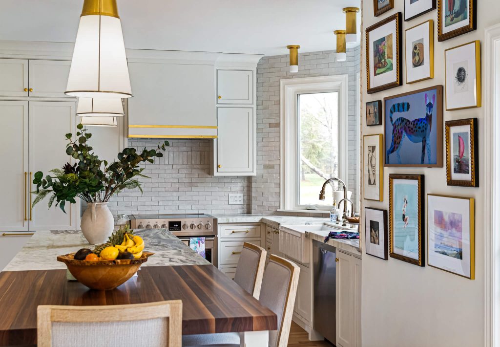 White kitchen with a walnut island top, a wall of framed art and a white range hood