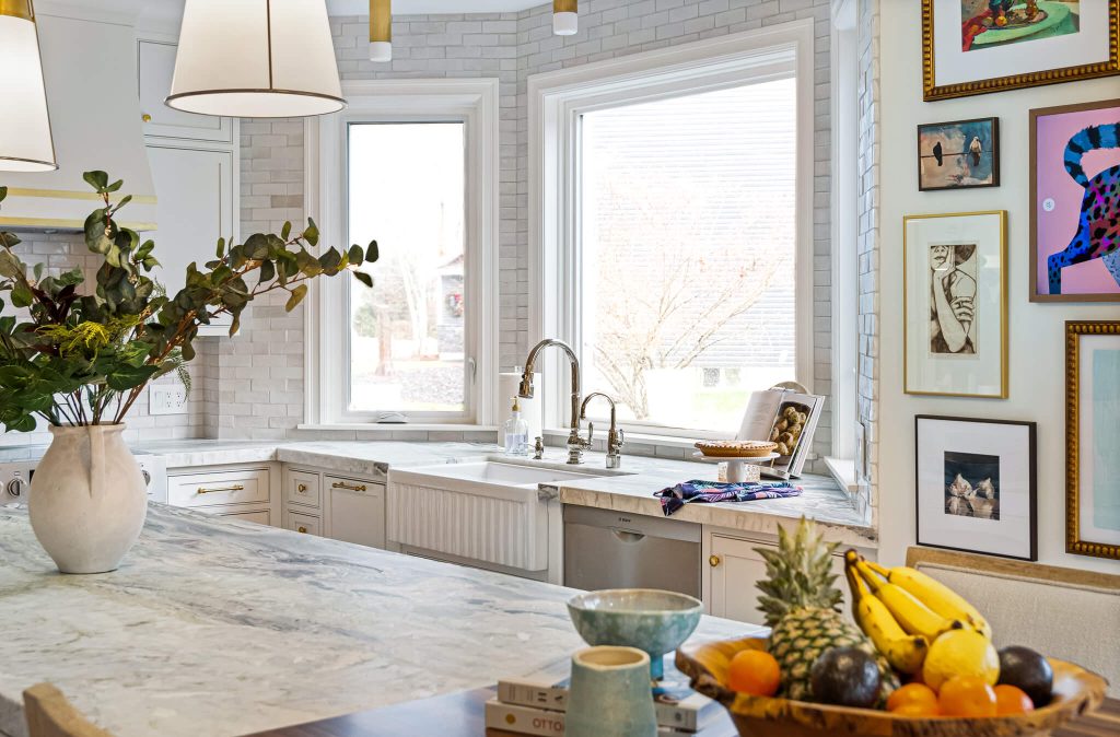 Marble island in a white kitchen facing a bay window and farmhouse sink