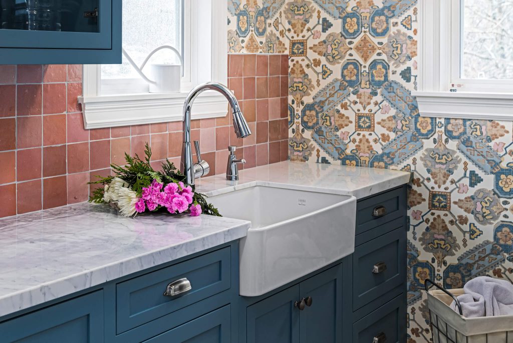 Teal cabinets with a marble counter and a farmhouse sink under a window