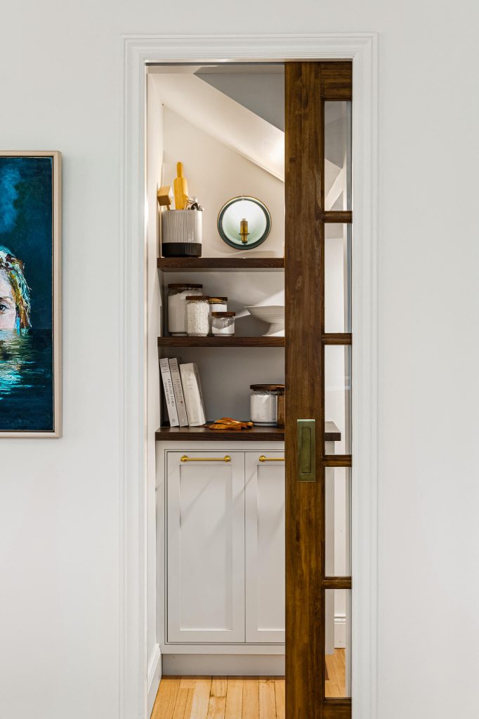 Walk-in pantry with open shelving seen through a walnut pocket door