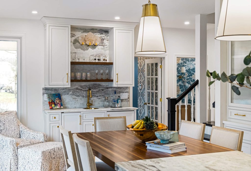 Coffee bar with white upper cabinets and an open walnut shelf beside a dining table